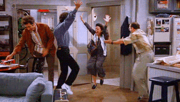 GIF of cast of Seinfeld doing a happy dance with their arms raised in an apartment