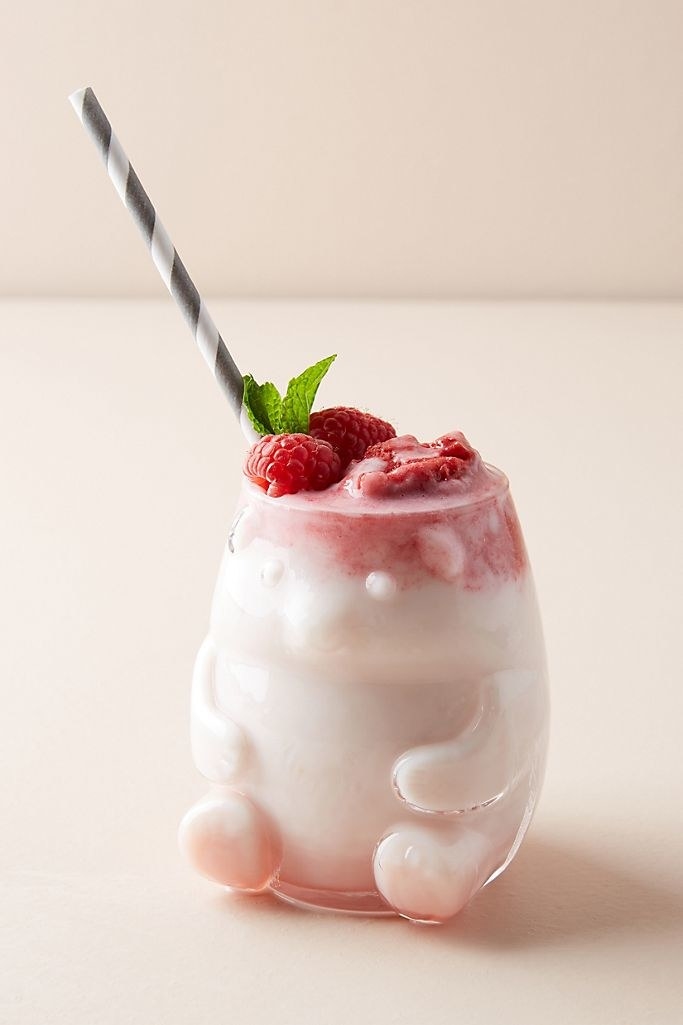 A bear shaped glass cup filled with a pink smoothie, raspberries, mint, and a striped straw