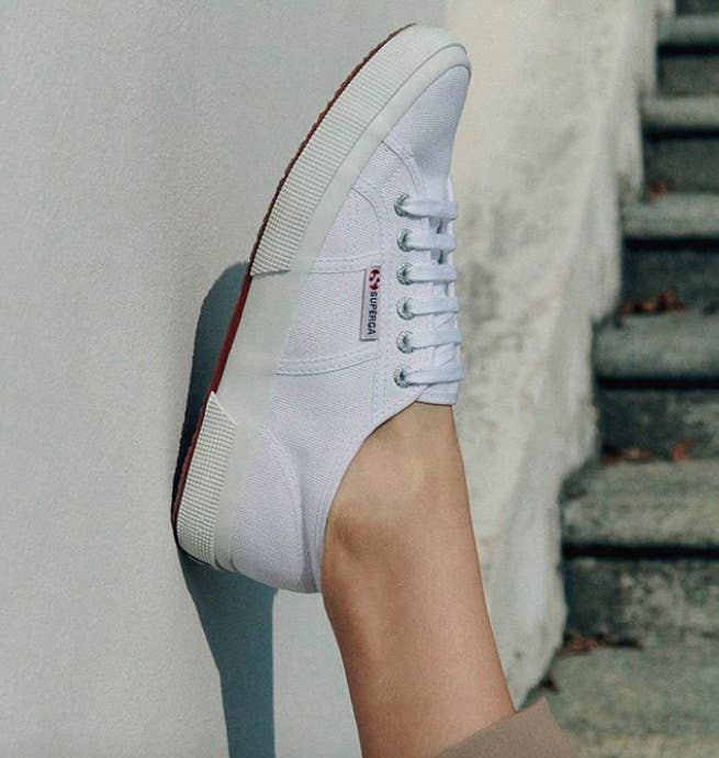 person placing their foot with a white Superga 2750 Cotu sneaker on it up against an outdoor wall