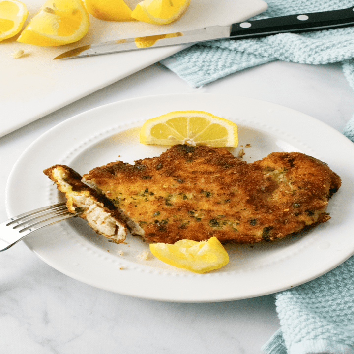 A fork and knife cutting into a crispy breaded chicken cutlet.