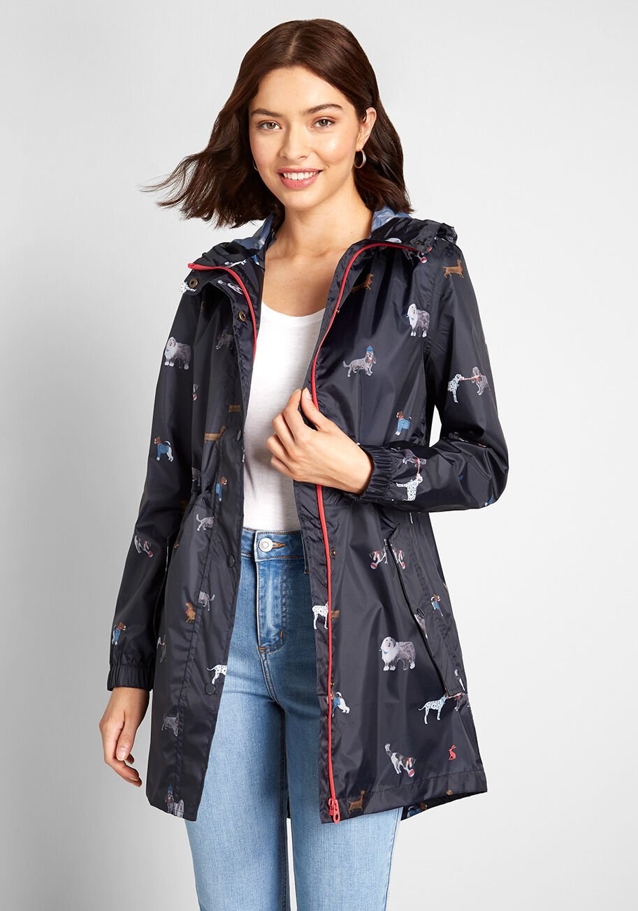A person wearing a hooded navy rain coat with an all-over dog print on it and a red zipper