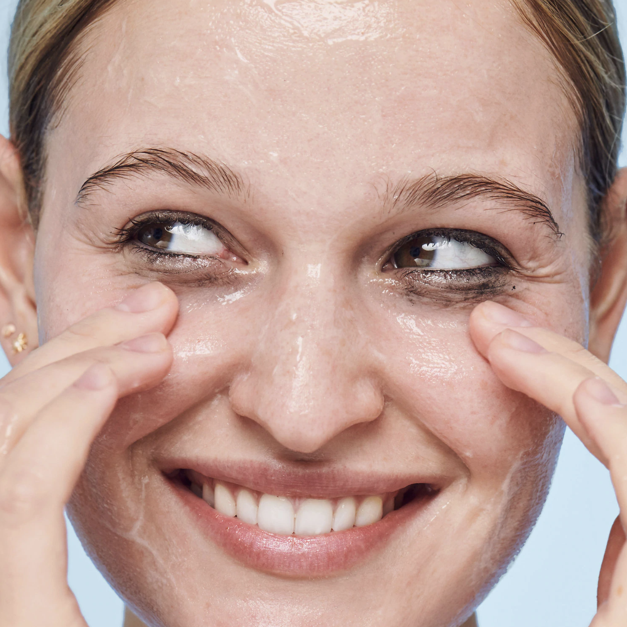 A person with the clear wash spread across their nose, forehead, and cheeks. The product is helping to remove the eyeliner from around the person's eye area