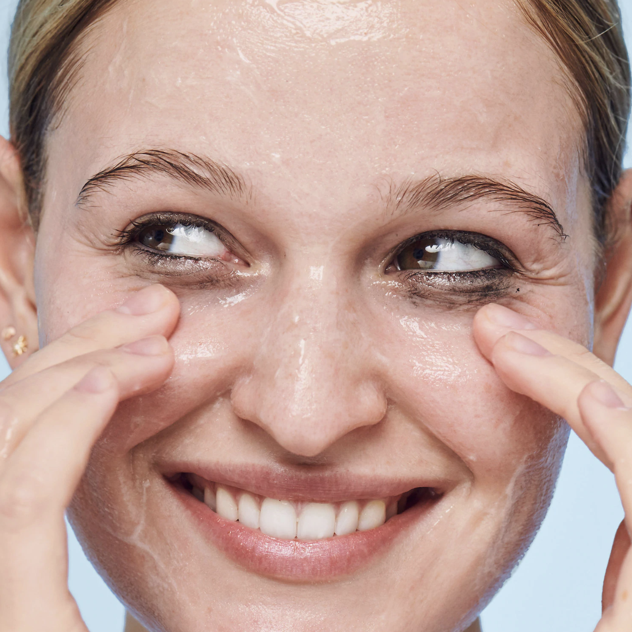 A person with the clear wash spread across their nose, forehead, and cheeks. The product is helping to remove the eyeliner from around the person&#x27;s eye area