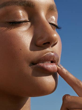 A model touches her lips after applying Glossier's Balm Dotcom skin salve