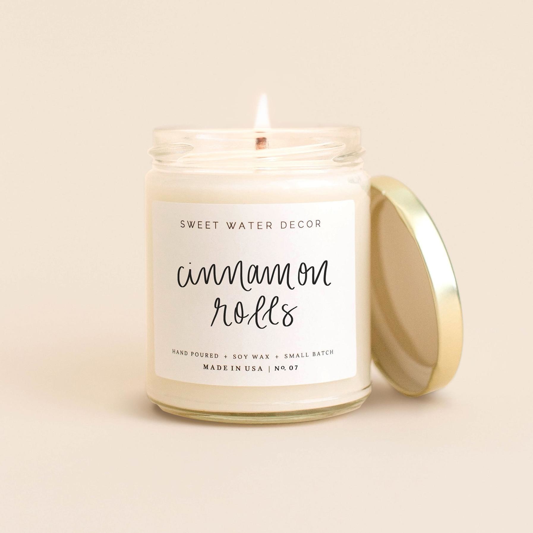 The all-white cinnamon roll candle lit in front of a neutral background