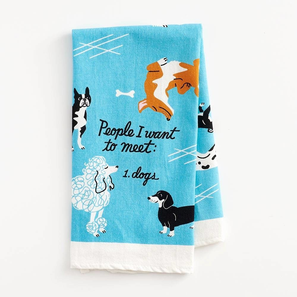 a bright blue tea towel with a white stripe on the bottom and dogs illustrated throughout with the saying &quot;people I want to meet: 1 dogs&quot;