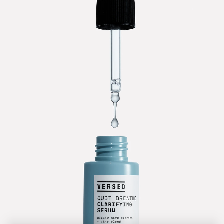 A blue bottle that says "Versed Just Breathe Clarifying Serum" with a dropper filled with transparent light blue liquid hovering over it