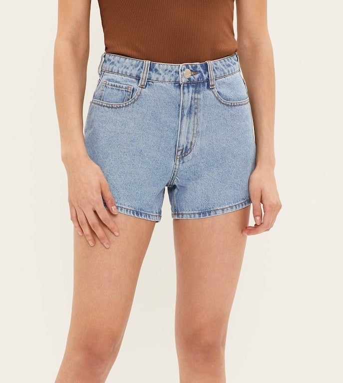 Model in light wash high waisted jean shorts that hit the upper mid thigh with a tucked in brown tank