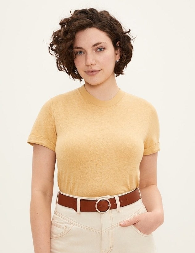 model in a tucked in light yellow crewneck tee with rolled sleeves styled with white denim and a brown leather belt