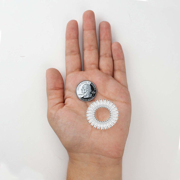 hand holding a white hair coil and a quarter to size. the colil is slightly larger
