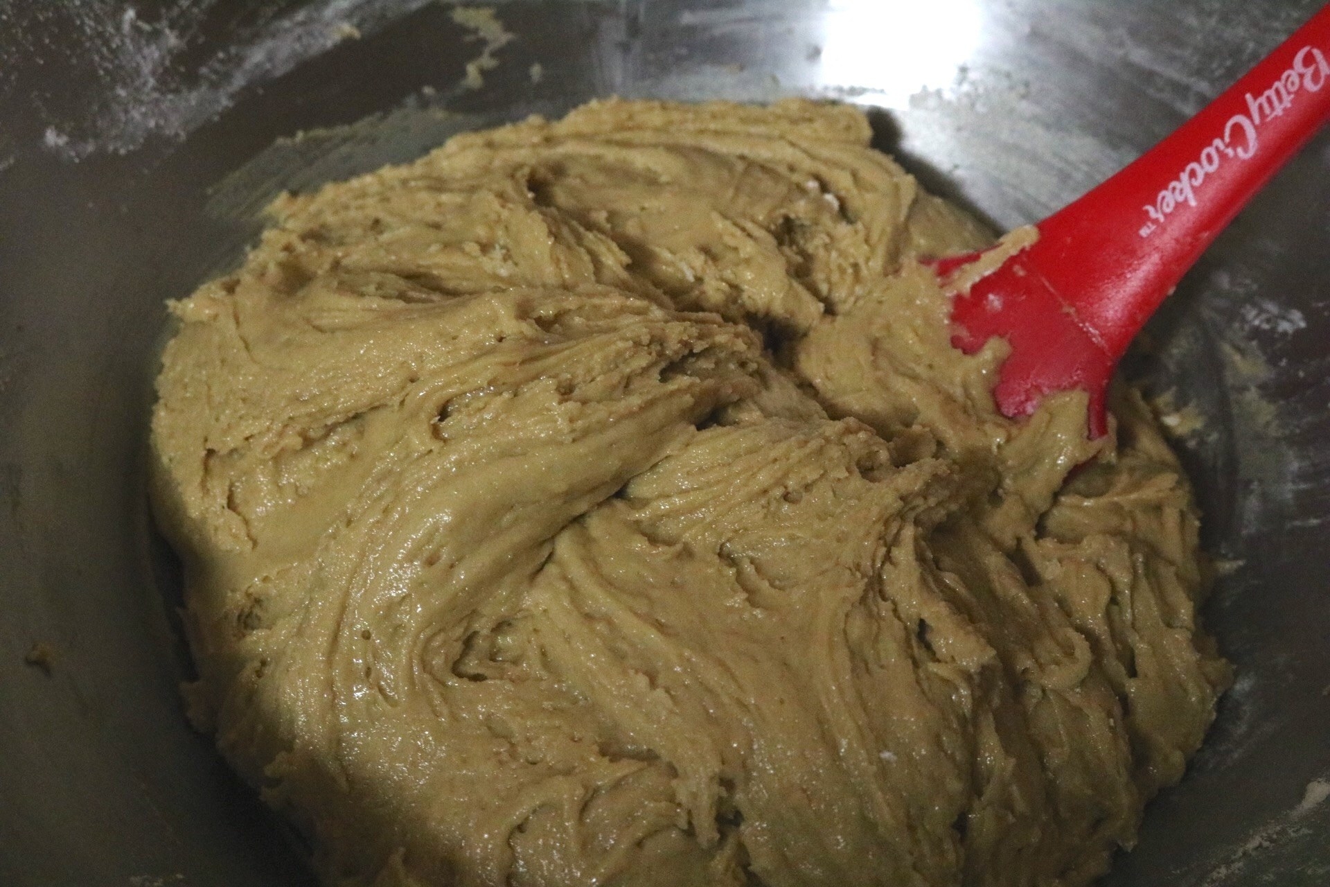 A medium shot of the bowl with the cookie dough inside. After adding vanilla, eggs, and the flour mixture, the dough looks thick and has taken on a darker color