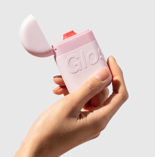 Model&#x27;s hand holding the pink hand cream, featuring the Glossier logo embossed on the outside