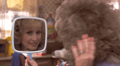 gif of Dolly Parton from the movie "Steel Magnolias" fixing her hair while looking into a hand mirror