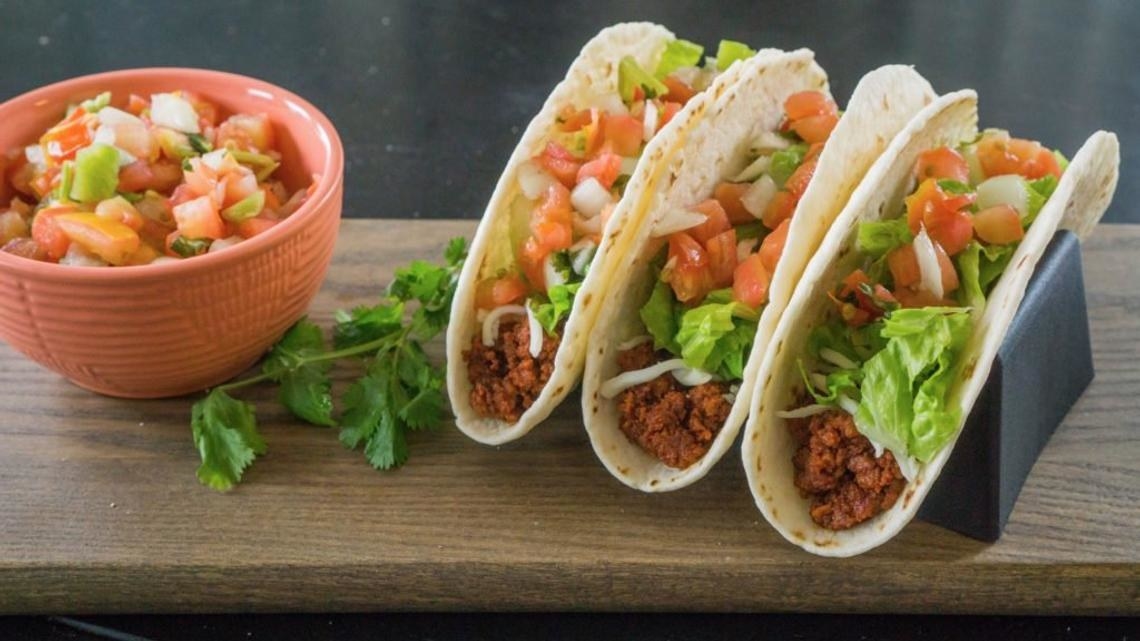 Three soft shell tacos held upright with a stand with three grooves in it