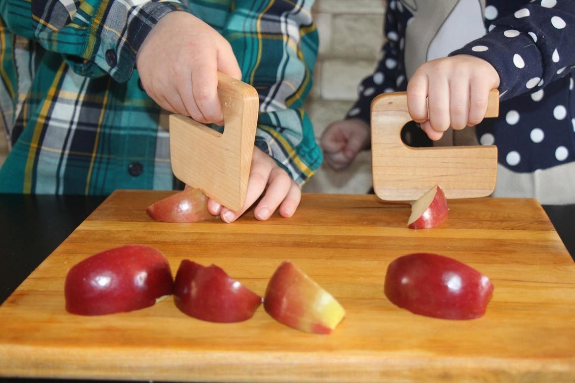 Two children using wooden blocks with handles to cut apples 
