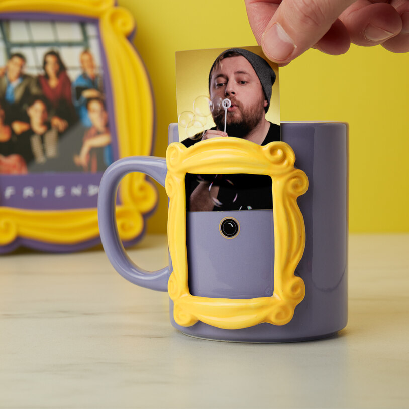 A person inserting a small photo into the signature yellow frame on the side of the mug