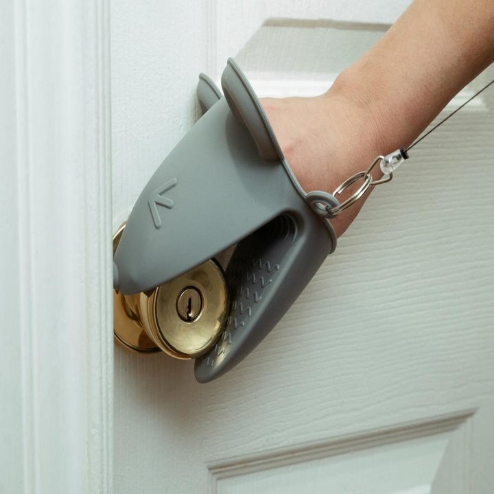 A hand wearing a silicone mitten shaped like a squinty mouse opens a door