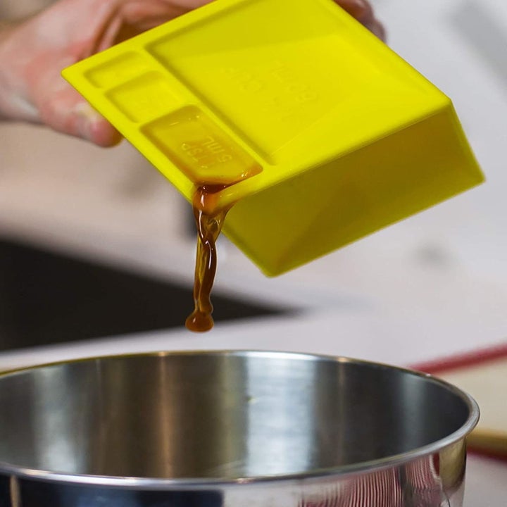 A person using one side of the cube to measure a liquid ingredient 