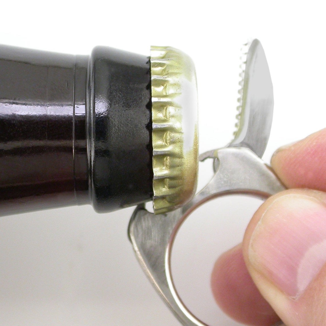 A silver ring with a knife popped out to expose a bottle opener. The ring is being used to open a beer bottle 