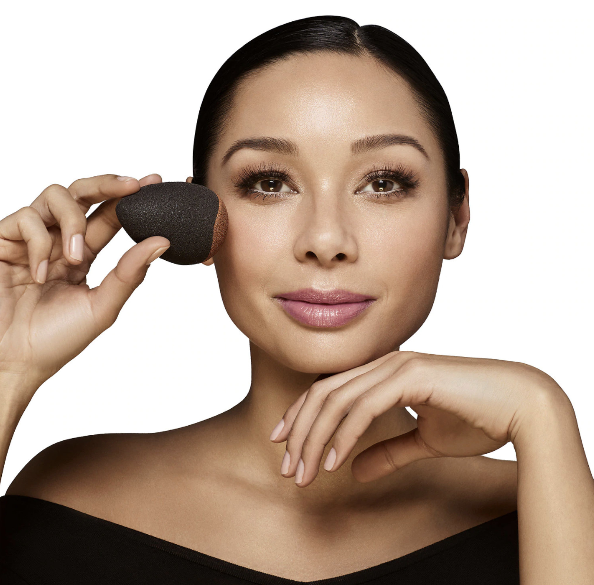 A model holding the black, egg-shaped beauty blender against their face