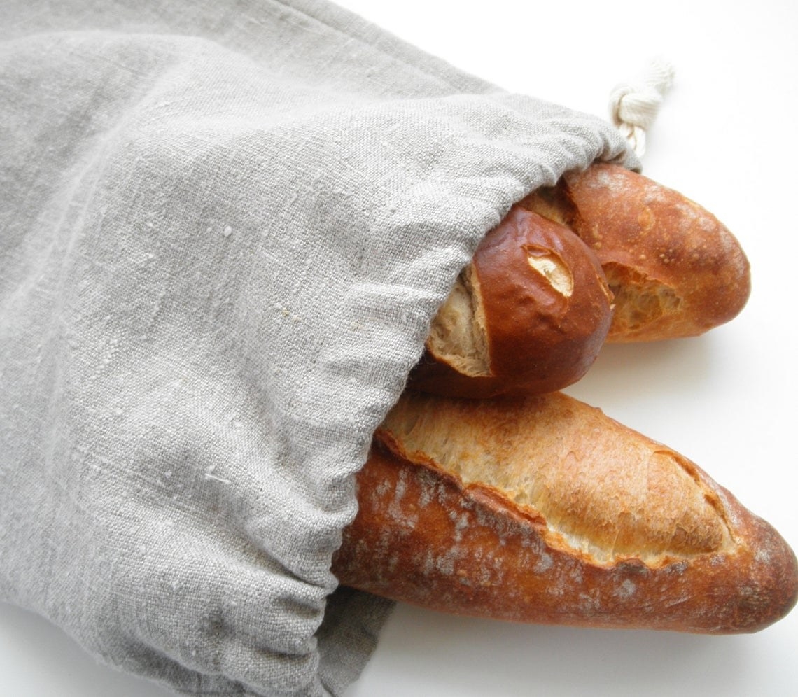 A light grey linen bag with a drawstring and three baguettes inside 