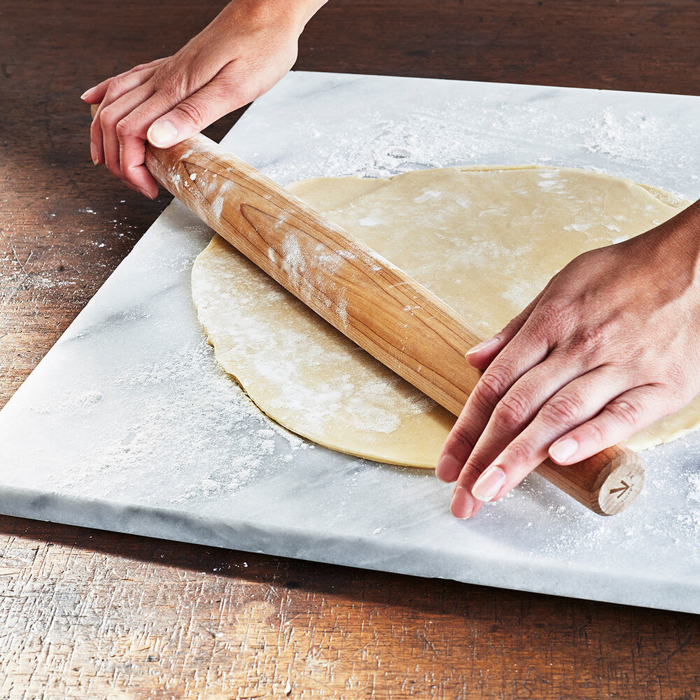 Hands using a rolling pin rolling dough on the board
