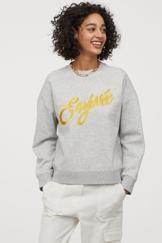 Smiling woman looking to the right wearing a grey sweater with gold text