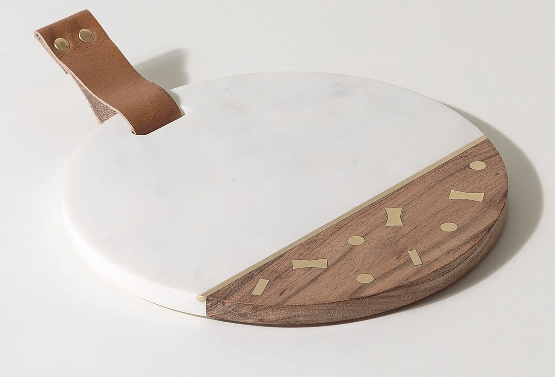 A white marble and wood chopping board with a leather handle and a gold-coloured metal strip separating the wood from the marble