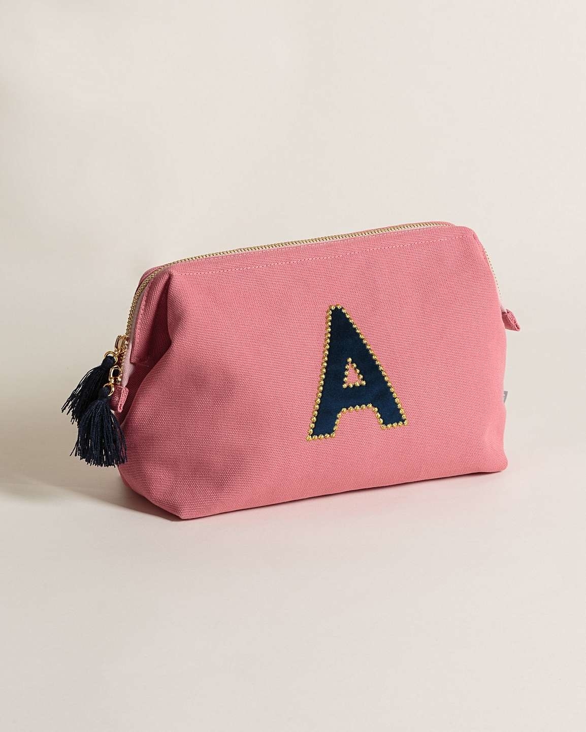 Pink velvet wash bag with a black letter "A" on it and black fringing on the zip