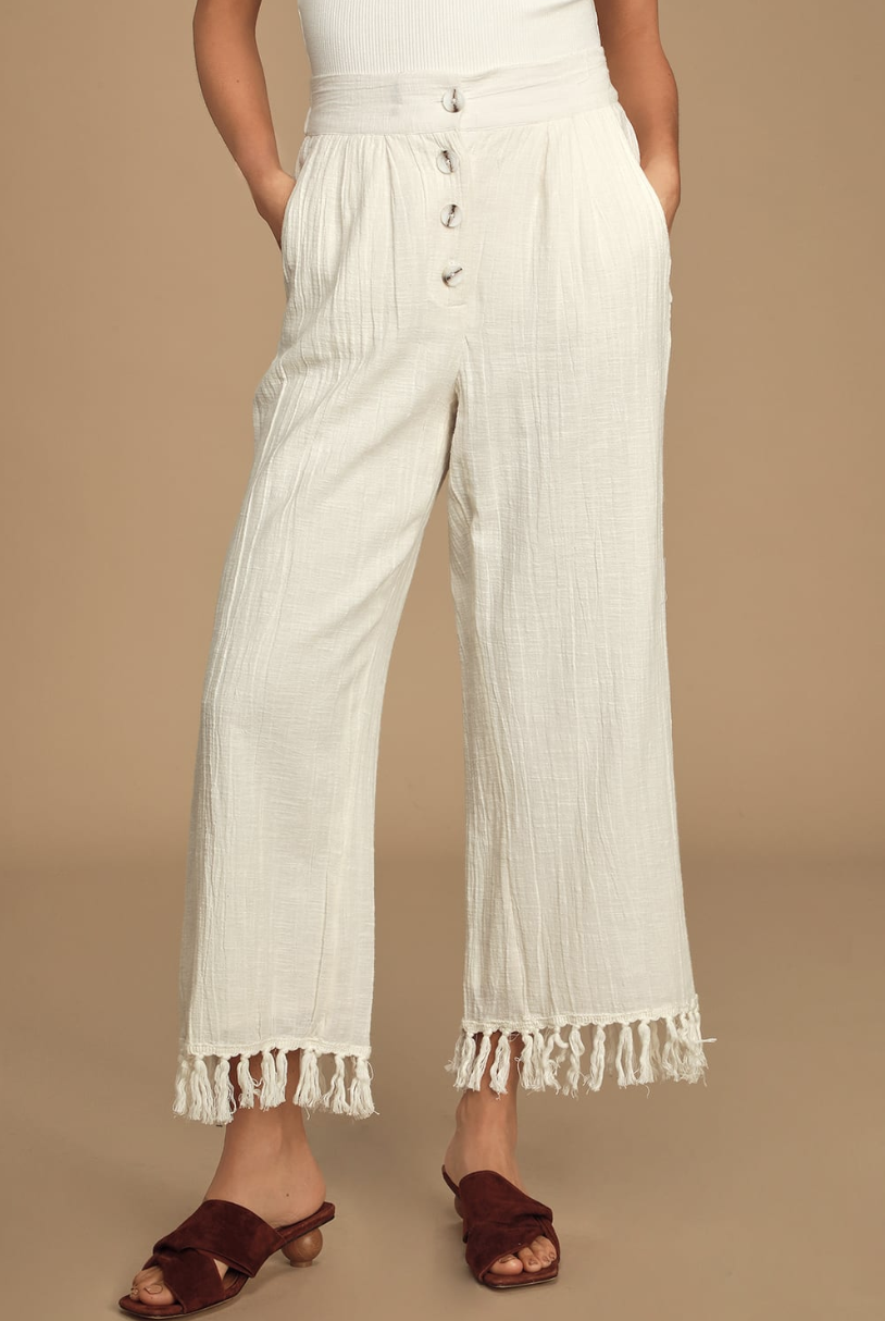 A waist-to-floor shot of the model wearing a pair of loose-looking white pants with a wide leg and tassels that hit their ankle