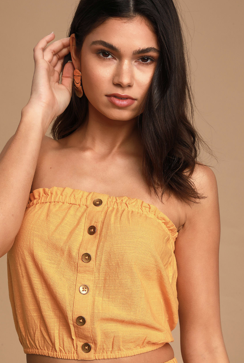 A medium shot of a model wearing the strapless crop top, which has a mustard yellow color and large buttons on the front