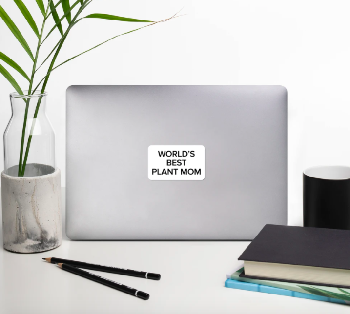 An open laptop with the top facing the camera and a sticker in the center that reads &quot;World&#x27;s Best Plant Mom&quot;