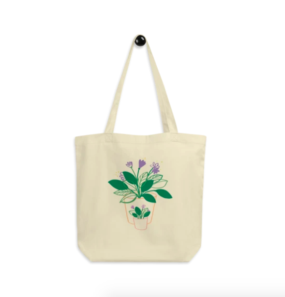 A cream tote bag with the illustration of two leafy plants with purple flowers on the front, one big, one small