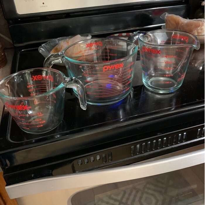 A set of three glass Pyrex measuring cups photographed atop a reviewer&#x27;s black stovetop