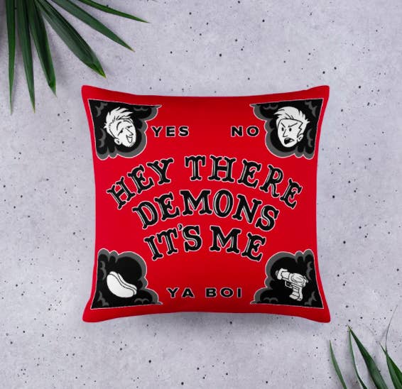 A red square pillow that is a spoof on a ouija board that says &quot;Hey There Demons It&#x27;s Me, Ya Boi&quot; on the center 