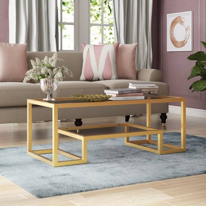 The table with gold metal trim, a glass top, and a shelf underneath it that also has a glass top and gold trim