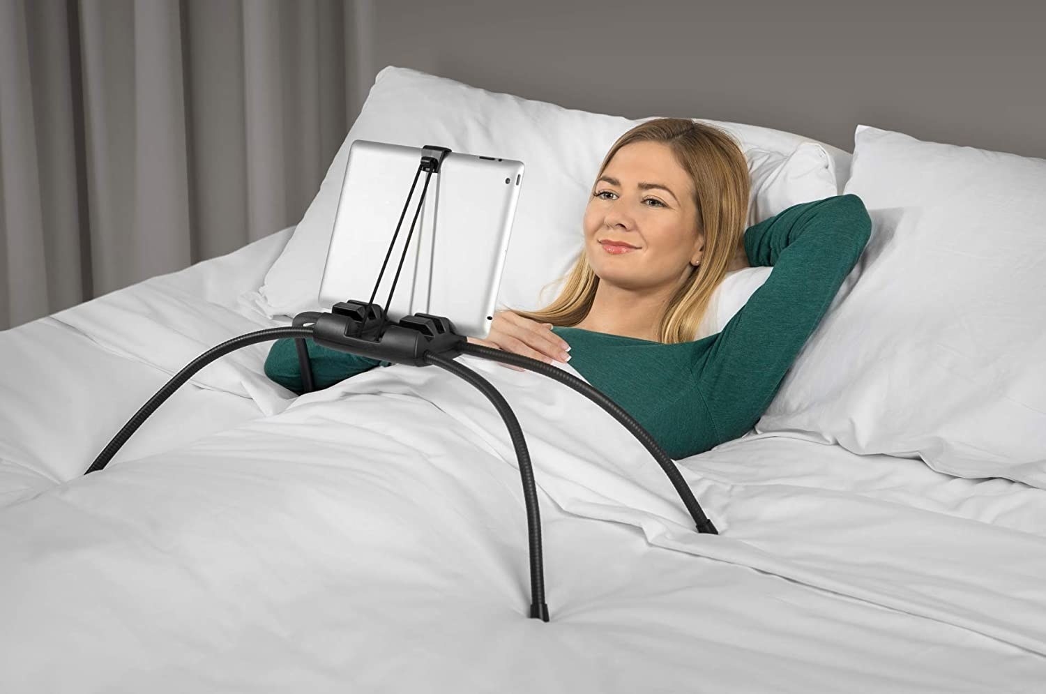 woman under the covers in bed with a tablet stand that has four bendable legs propped up on the bed so she can look at the screen without holding it