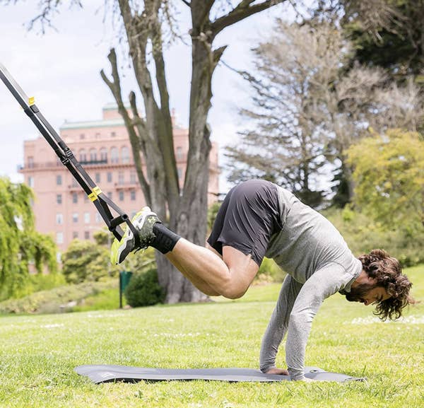A model completes a pike movement with the TRX GO Suspension Training system above a mat outside