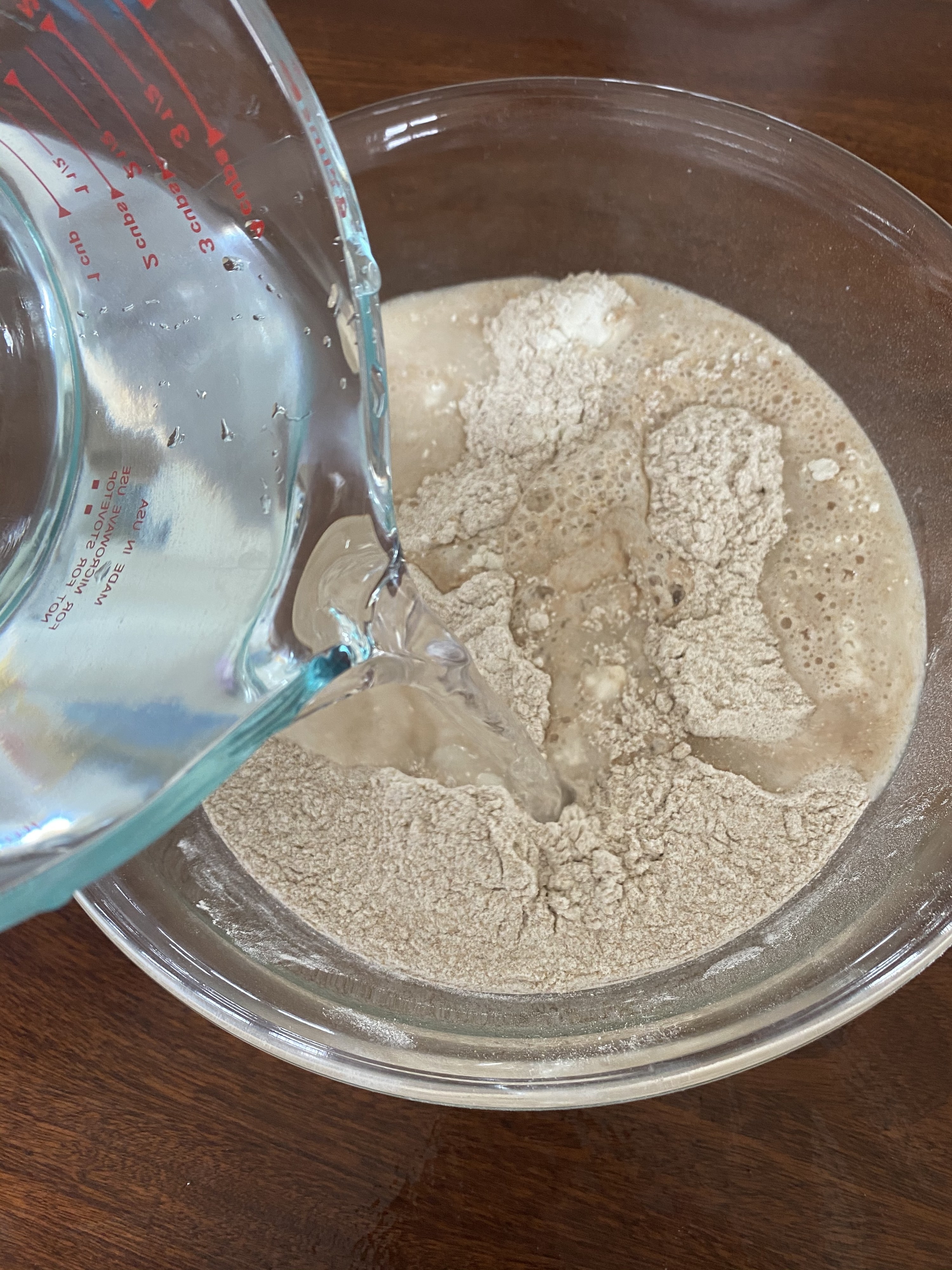 Water being poured into a bowl of flour to prepare the autolyse.