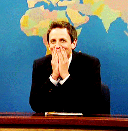 Seth Meyers holding his hands up to his mouth trying not to laugh 