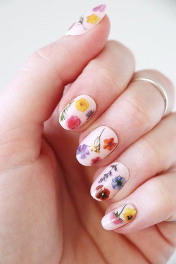 A person displaying their painted fingernails with tiny flower tattoos on top of the nails