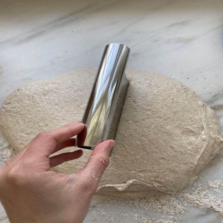 A ball of dough being sliced into two with a bench scraper.