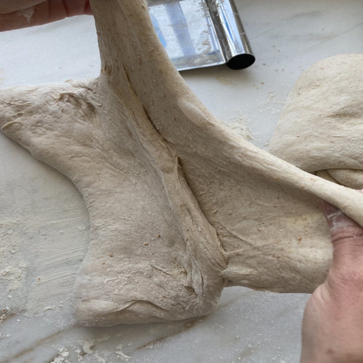 Hands folding a square of dough from right to left.