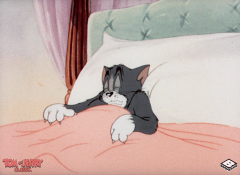 A gif of Tom from the cartoon "Tom and Jerry" yawning and relaxing in bed