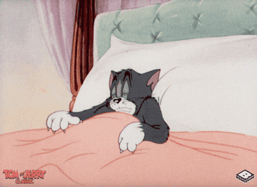 A gif of Tom from the cartoon &quot;Tom and Jerry&quot; yawning and relaxing in bed