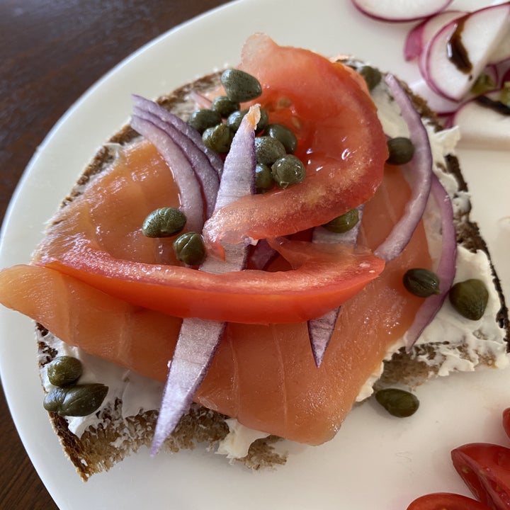 A slice of sourdough bread with cream cheese, lox, capers, onion, and tomato.