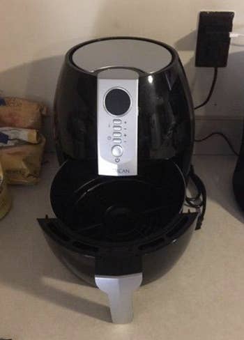 Air fryer appliance with several buttons indicating cooking settings and its bottom part open to show where the food goes before you slide it back in to cook 