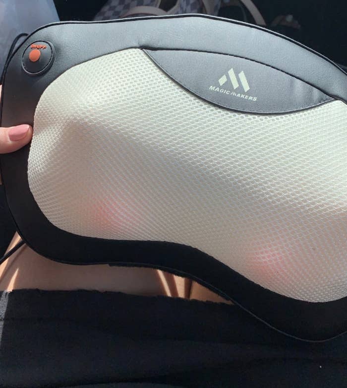 A reviewer holding the massager, which has three rotating heated balls under the fabric on both sides