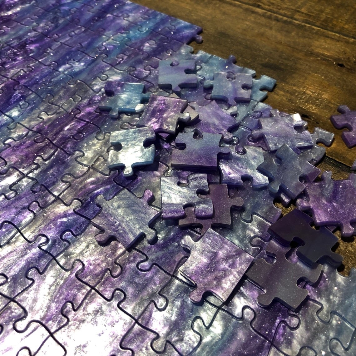 holographic purple and silver jig saw puzzle with some connected and some loose pieces. No decipherable patten on puzzle, so it would be difficult