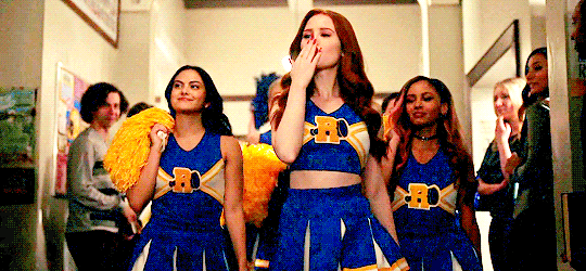 Three cheerleaders from "Riverdale" walking down a hallway blowing kisses.